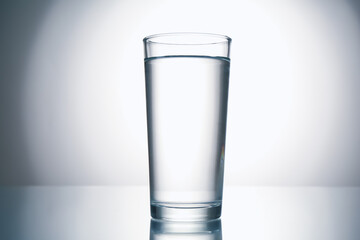Fresh water in glass on mirror table against gray gradient background