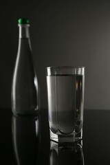 Fresh water in glass and bottle on mirror table against gray background, selective focus
