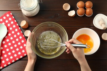 Woman whisking egg whites in bowl at wooden table, top view