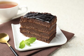 Piece of chocolate cake served with mint, spoon and tea on white table, closeup