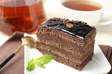 Piece of chocolate cake served with mint, spoon and tea on table, closeup