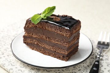Piece of chocolate cake served with mint and fork on table, closeup
