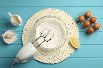 Hand mixer with whipped cream, eggs and other products on light blue wooden table, flat lay