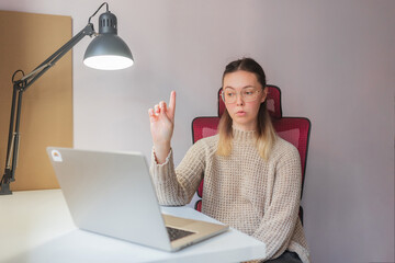 Woman raising finger, appearing to explain something during video call.	Confident gesture and...