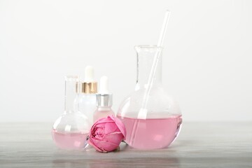 Making luxury perfume. Essential oils in glassware and flowers on white wooden table, closeup