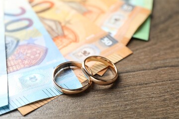 Gold wedding rings and euro banknotes on wooden table, closeup