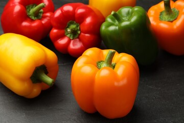 Fresh colorful bell peppers on black textured table, closeup