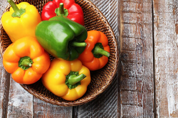 Fresh colorful bell peppers in wicker basket on wooden table, top view