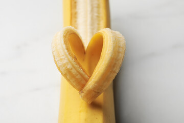 Banana with heart made of peel on white table, closeup