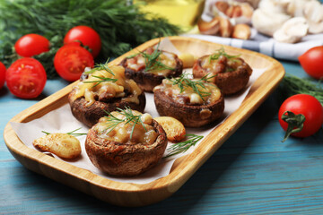 Delicious stuffed mushrooms with melted cheese, garlic and dill on light blue wooden table, closeup