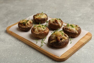 Delicious stuffed mushrooms with melted cheese and thyme on grey textured table, closeup