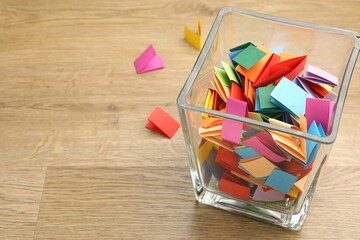 Jar with colorful pieces of paper on wooden table, closeup. Space for text