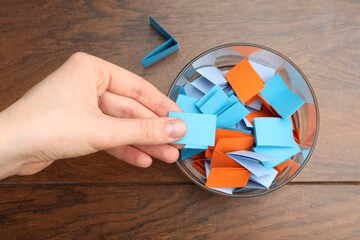 Woman taking paper with message out of jar at wooden table, top view