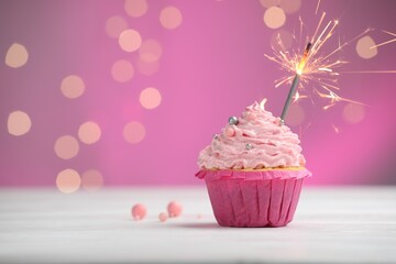 Burning sparkler in cupcake on table against pink background with blurred lights. Space for text