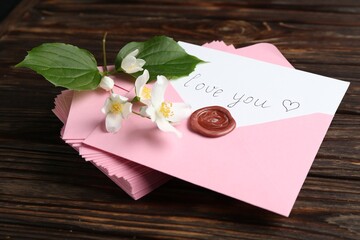 Letter with phrase I Love You, envelopes and beautiful flowers on wooden table, closeup