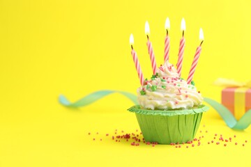 Burning candles in cupcake, sprinkles and party decor on yellow background, space for text