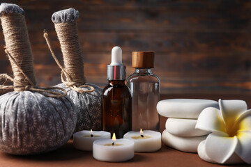 Massage bags, stones, cosmetic products, burning candles and plumeria flower on dark beige table,...