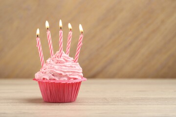 Burning candles in cupcake on wooden table, space for text