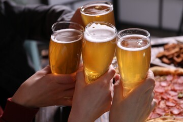 Friends clinking glasses of beer at table, closeup