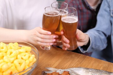 Friends clinking glasses of beer at wooden table, closeup