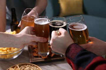Friends clinking glasses of beer at white wooden table, closeup