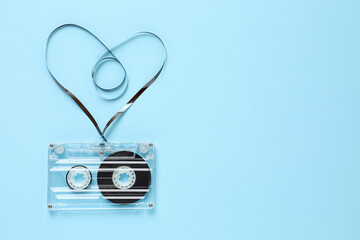 One audio cassette with heart shaped magnetic tape on light blue background, top view. Space for...