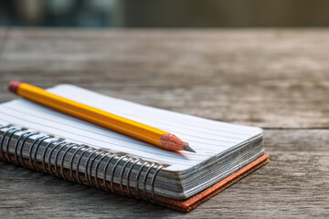 A yellow pencil lies atop a spiralbound notebook resting on a textured wooden surface