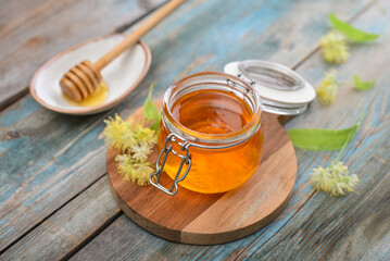 Linden honey in glass jar with wooden honey dipper