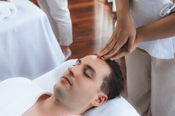 Fototapeta na wymiar Caucasian man enjoying relaxing anti-stress head massage and pampering facial beauty skin recreation leisure in dayspa modern light ambient at luxury resort or hotel spa salon. Quiescent