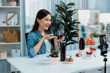 Smiling young beautiful Asian reviewing tasty mixed strawberry and cherry juice detox drinks,...