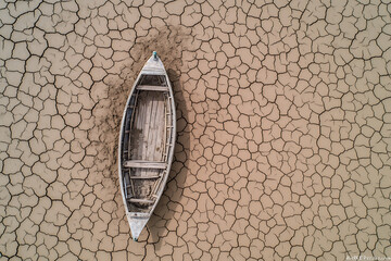 Abandoned boat sits stranded on cracked earth, a stark symbol of drought and environmental challenges. The desolate landscape conveys a powerful message.