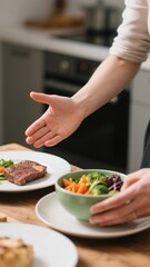A close up view of a person placing a bowl of cooked vegetables next to a plate with a juicy steak, offering a balanced meal to someone with an outstretched hand