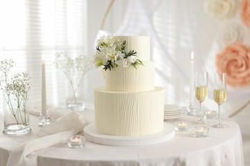 Delicious wedding cake with floral decor and glasses of champagne on table indoors