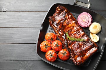 Delicious roasted pork ribs with rosemary, tomatoes and onions on grey wooden table, top view. Space for text