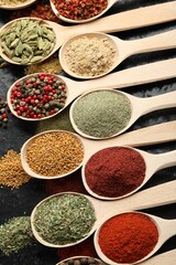 Many different spices in spoons on black table, flat lay