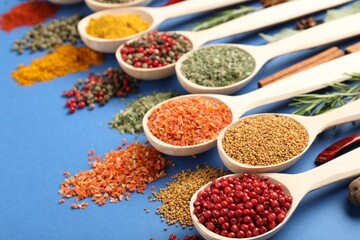 Different aromatic spices in spoons on blue background, closeup