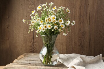 Beautiful chamomile flowers in glass vase on wooden table