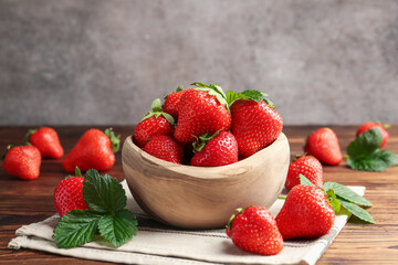 Fresh ripe strawberries and leaves in bowl on wooden table, closeup
