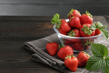Fresh ripe strawberries and leaves in container on black wooden table, closeup. Space for text