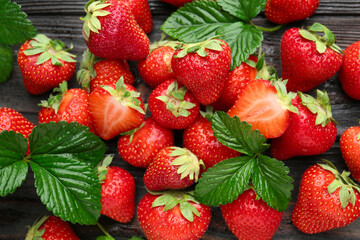 Fresh ripe strawberries and leaves on black wooden table, flat lay