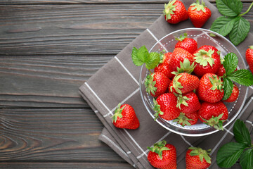 Fresh ripe strawberries and leaves in container on black wooden table, flat lay. Space for text
