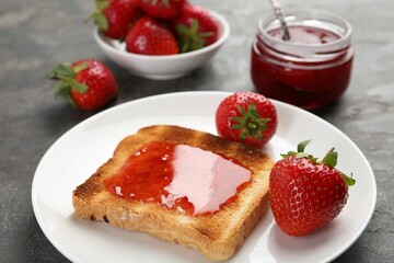 Toast with tasty homemade strawberry jam and berries on grey table, closeup