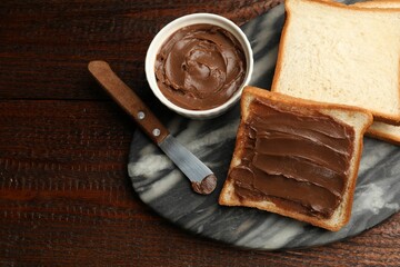 Sandwiches with chocolate butter and knife on wooden table, flat lay