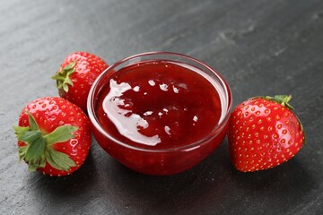 Tasty homemade strawberry jam and berries on black table, closeup