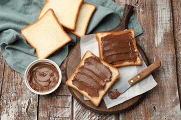 Sandwiches with chocolate butter and knife on wooden table, flat lay
