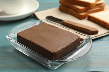 Block of tasty chocolate butter in glass keeper on light blue wooden table, closeup