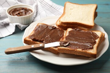 Pieces of bread with tasty chocolate butter and knife on light blue wooden table, closeup