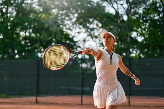Confident female tennis player hitting forehand shot on clay court