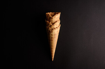 Three waffle cones are stacked neatly against a dark backdrop, awaiting tasty ice cream scoops and...