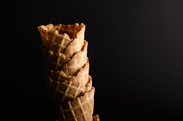 Stack of multiple waffle cones displaying intricate textures, set against a dark backdrop,...